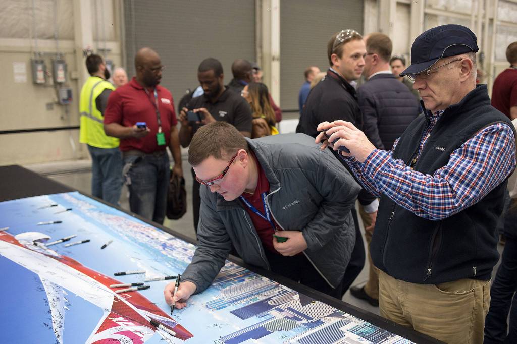 Boeing employees sign and take photos of a poster bearing an image of the new 777X while attending a gala at the composite wing center on Monday. (Dave Rzegocki / For the Herald)