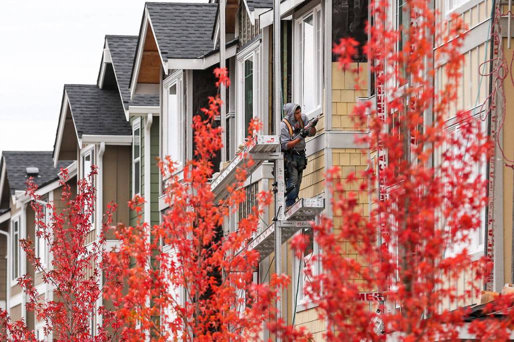 A construction worker caulks the siding on a townhouse at The Towns at Riverfront housing development in Everett on October 25, 2017. (Kevin Clark / The Herald)