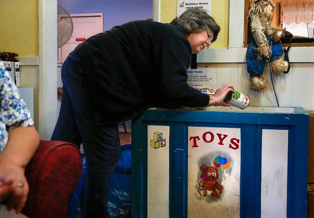 Matthew House volunteer Karol Bentley looks over canned food kept in a large wooden toy box in the Welcome Room. (Dan Bates / The Herald)