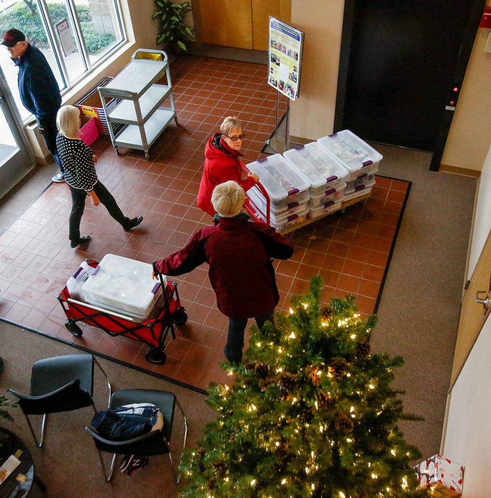 Assistance League of Everett volunteers bring items into the lobby and elevator to prepare for a holiday crafters marketplace in the spacious upstairs at the groups 5107 Evergreen Way building in early November. From left they are David Gunderson, president Carla Hogan, Linda Wardlow, (bright red) and Happi Favro (nearest). (Dan Bates / The Herald)