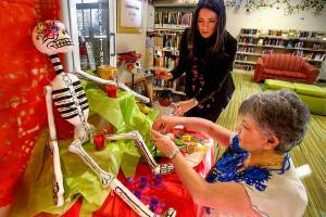 At Lynnwood Library, Julieta Altamirano-Crosby (left) and Maria Casey create a Day of the Dead display in the childrens area Tuesday. The women created a larger adult version as well. (Dan Bates / The Herald)