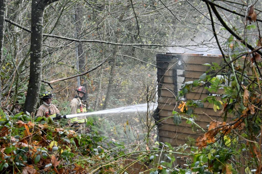 Firefighters and Snohomish County sheriffs deputies work at a home where a man was found dead in the garage after a house fire Wednesday morning. (Caleb Hutton / The Herald)