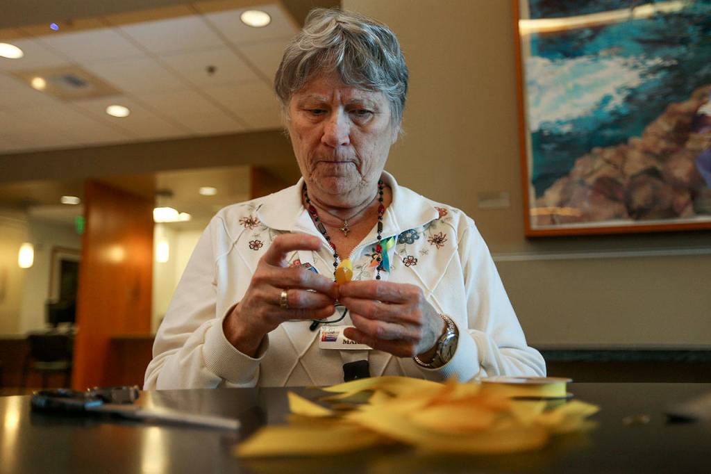 American Cancer Society volunteer Marilee Richards makes yellow ribbons, the color symbolizing sarcoma bone cancer, while working at the information desk at the Cancer Resource Center at Providence Regional Medical Center on Oct. 31 in Everett. (Andy Bronson / The Herald)