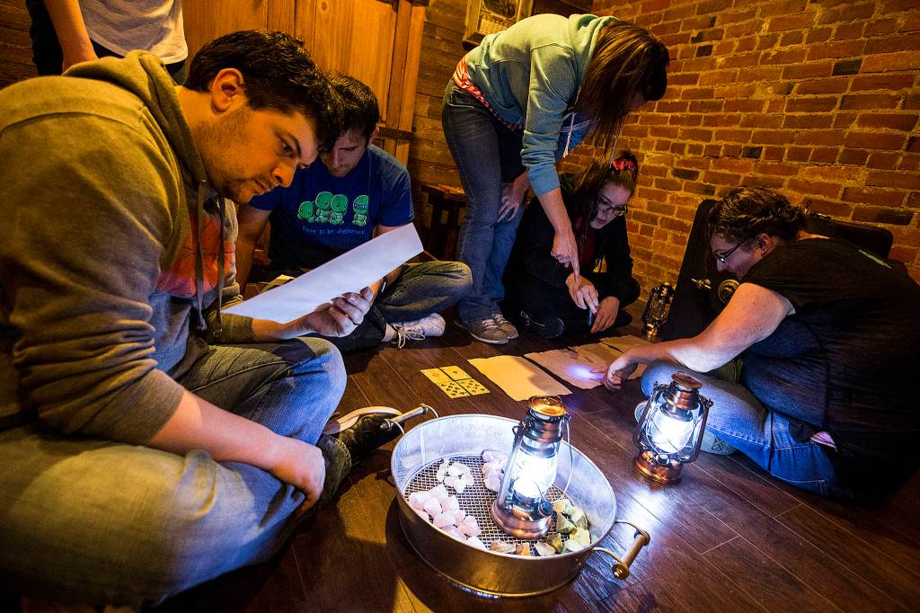 Brian Flansburg (left) looks for clues in a document while his friends try and decode other messages at the Escape Scene in downtown Everett on May 6. (Ian Terry / The Herald)
