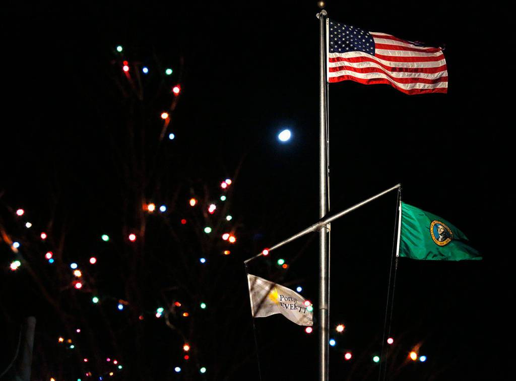 The extra (bigger) Christmas light is the moon from behind flags outside offices at the Port of Everett on Tuesday evening. (Dan Bates / The Herald)