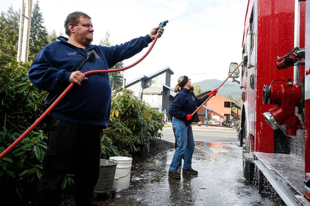 Darrington firefighter Larry Schoder (left) rinses off a fire engine on Tuesday, Dec. 12. Schoder and his wife, Kris, are both volunteers at the station. (Ian Terry / The Herald)