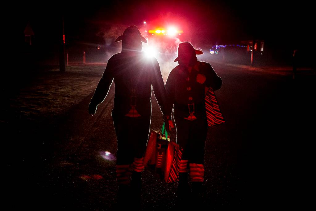 Silhoutted by the lights of a fire truck, Darrington volunteer firefighters Angela Botamanenko and Tim Ziesemer walk through town on Tuesday, Dec. 12 while handing out candy canes for the annual Christmas Parade. (Ian Terry / The Herald)