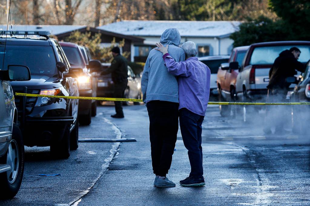 A man and woman embrace as they look toward a home where a 54-year-old woman was shot and killed Dec. 7 in the Village Green Mobile Home Park in south Everett. (Ian Terry / The Herald)