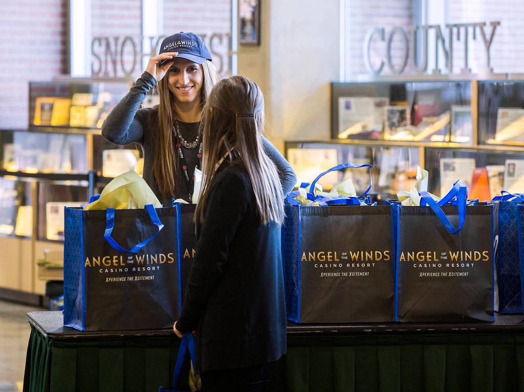 Amanda Strong (left) tries on an Angel of the Winds Arena hat as she and Courtney Brown hand out gift bags after the renaming ceremony Dec. 13 in Everett. The new name replaces the Xfinity name. (Andy Bronson / The Herald)