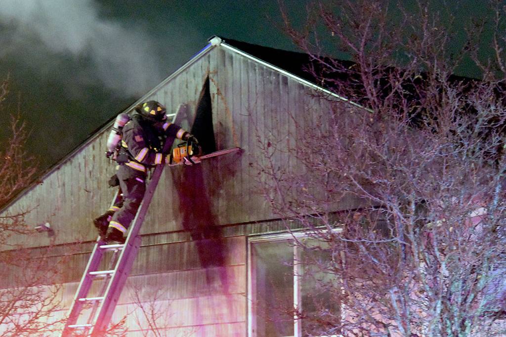 Crews climbed ladders with chainsaws to cut through walls to extinguish hot spots in the attic at an apartment building fire in Everett Thursday night. (Caleb Hutton / The Herald)