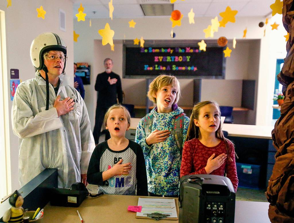 Dressed for a big day of space exploration Feb. 16, Highland Elementary principal Ryan Henderson enlists (from left) third-grader Harmony Piffath, second-grader Camrie Ingram and third-grader Makayla Goshorn to help lead the pledge over the intercom for the whole school. (Dan Bates / The Herald)