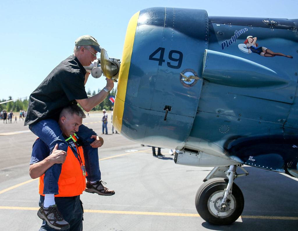 George Slocum sits on Brandon Edwards shoulders as he wipes down a propellor during the Arlington Fly-In at Arlington Municipal Airport in Arlington on July 8. (Kevin Clark / The Herald)