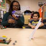 Lowell Elementary teacher Erin Marrow uses a blow dryer to represent the Big Bad Wolf to move a straw house across the table as Giovanni De Jesus Olmos watches Thursday in Everett. Using the theme of The Three Little Pigs, early learning students use STEM practices to build and test model houses built from straws, popsicle sticks and LEGO bricks. (Andy Bronson / The Herald)