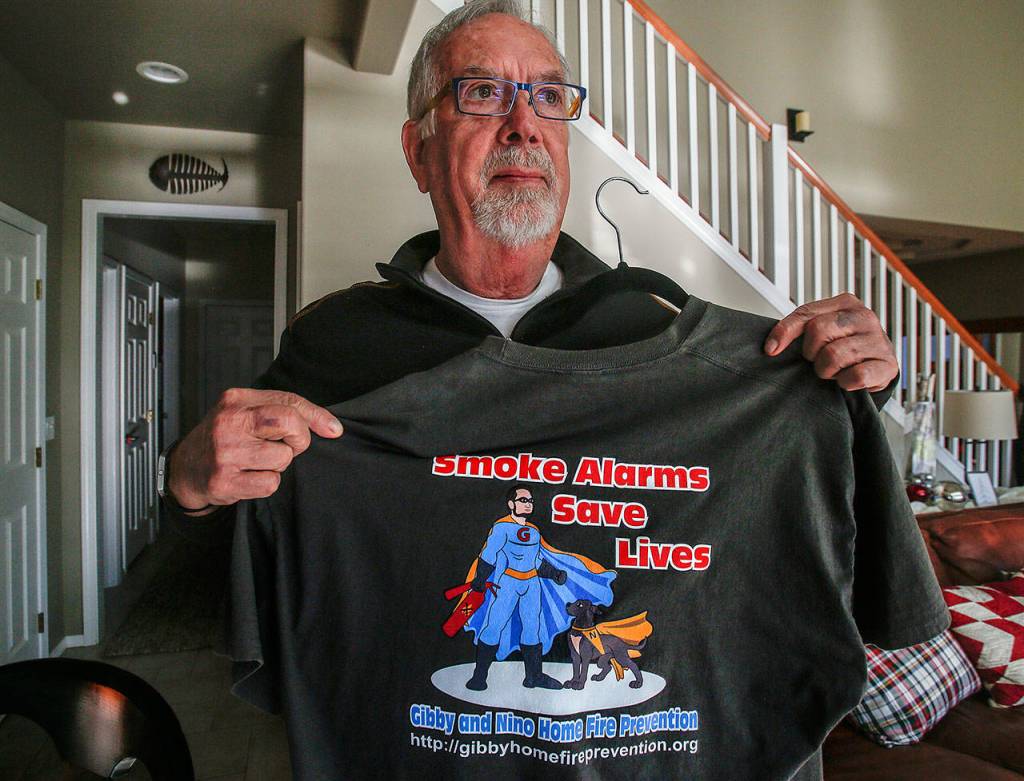 Gerry Gibson holds a T-shirt bearing his and Bonnies nonprofit company message and logo with Gibby and his dog, Nino, as the heroes. The Gibsons are urging lawmakers to change state law regarding wrongful death suits. (Dan Bates / The Herald)