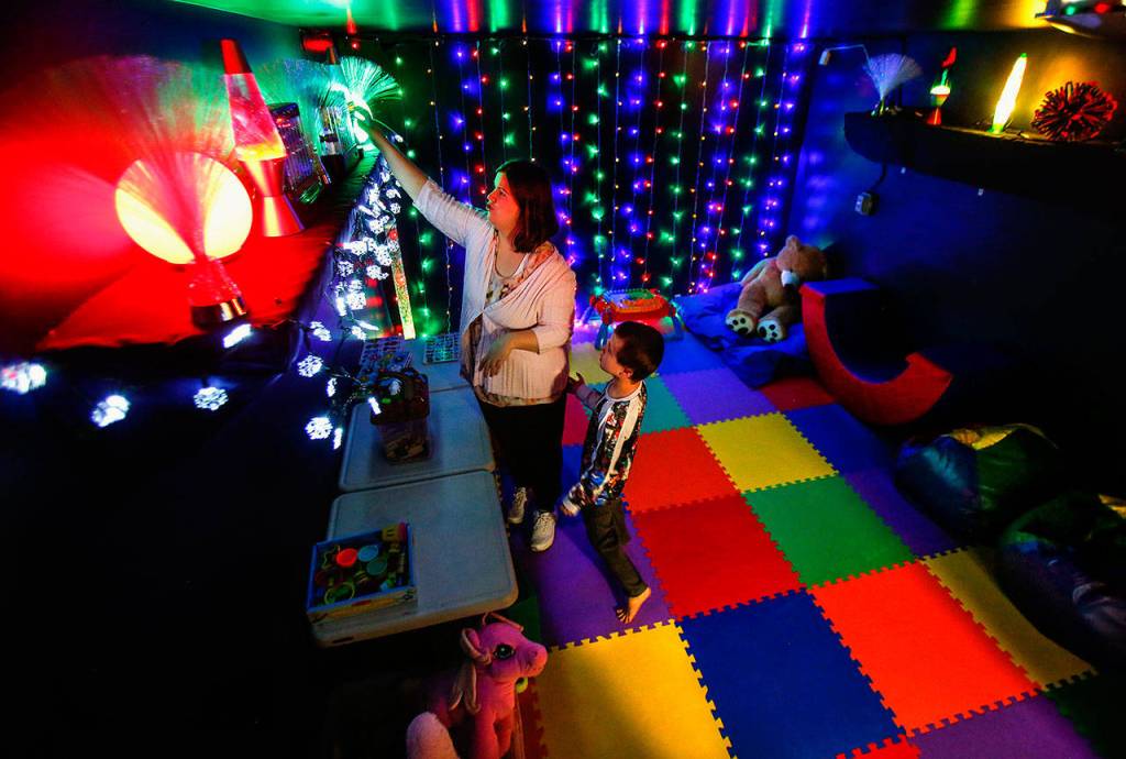 Breanna Standley, 25, reaches for an artificial aquarium in Wee Fits sensory room while her son Hunter, 6, waits to get his hands on it. (Dan Bates / The Herald)