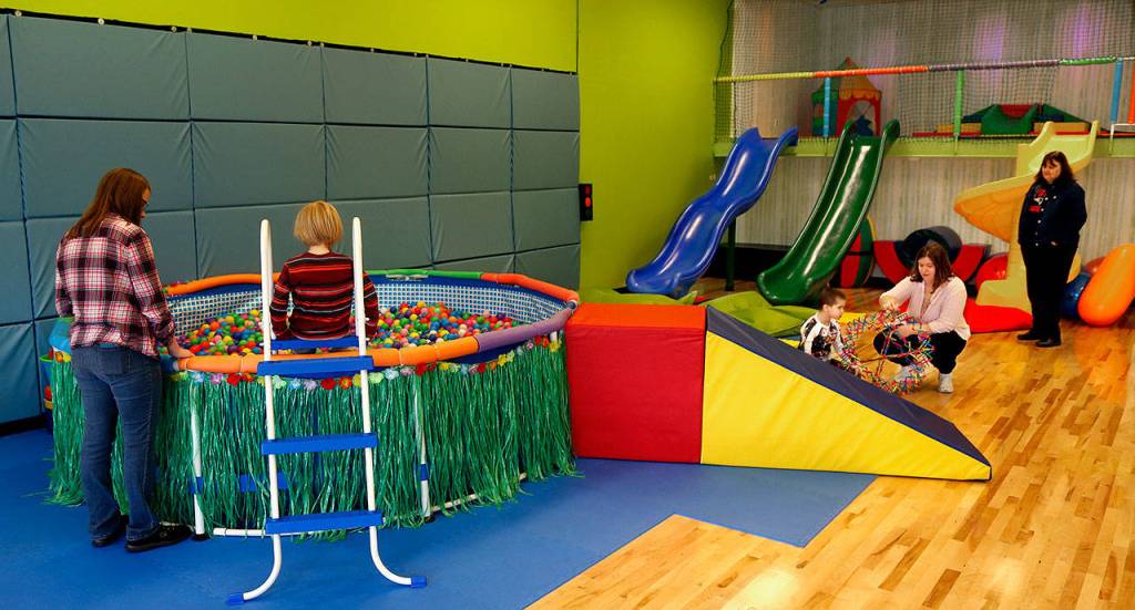 Volunteer Metia Napier, 20, (left) watches and talks with a young boy who is contemplating a jump into a small swimming pool filled with plastic balls Friday at Wee Fit in Everett. Napier, from Everett, has three brothers with autism. (Dan Bates / The Herald)