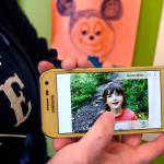 Wee Fit co-owner Melissa Wren holds up a cellphone picture of her son, Cooper, 6, who has autism. Pictures drawn by Cooper are hanging in several places around Wee Fit. (Dan Bates / The Herald)