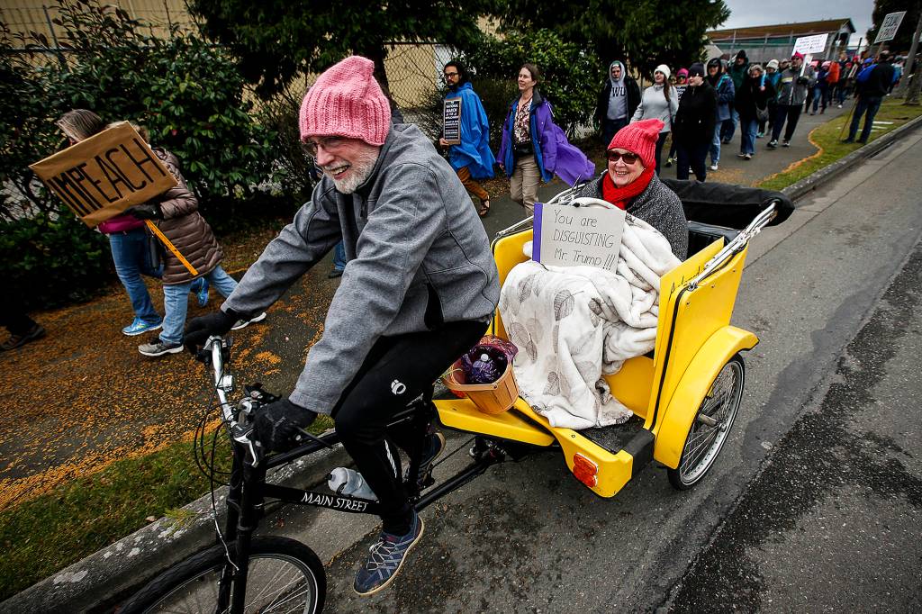 Tim and Kathy Tobin, of Everett, ride their pedicab along with others participating in the March to Impeach on 10th Street near West Marine View Drive in Everett on Saturday. Demonstrations are being held across the country Saturday and Sunday to protest President Donald Trump on the 1-year anniversary of his inauguration. (Ian Terry / The Herald)