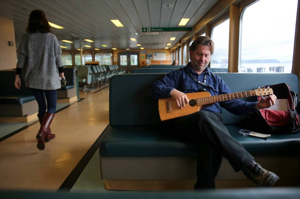 Dave Christian plays his travel guitar aboard a ferry headed to Mukilteo on a recent morning. (Kevin Clark / The Herald)