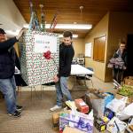 Jason Swift (left) carries a box full of donated presents with Brandon Wright as fellow volunteers Christina Thomas and Jamie Wright help organize other gifts at the Mukilteo Chamber of Commerce building on Tuesday, Dec. 19. The program, Mukilteo Love, was started by Shana Swift and is expected to help provide gifts to over 60 local children in need this holiday season. (Ian Terry / The Herald)