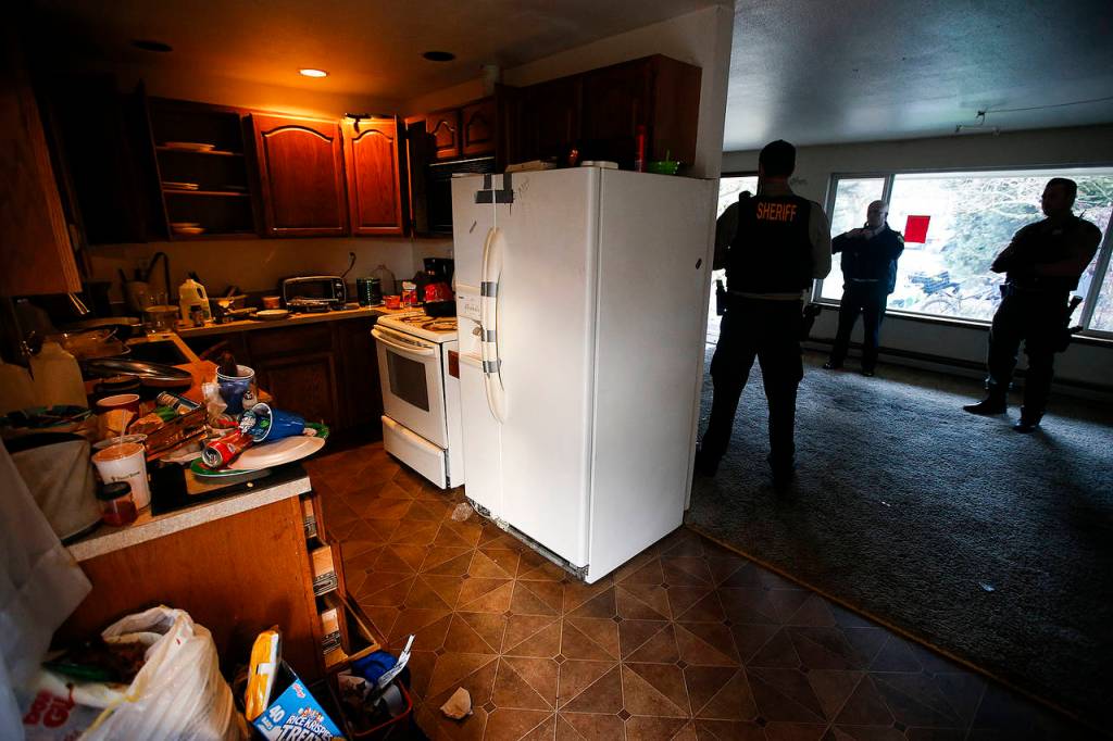 Snohomish County Sheriffճ deputies stand in the cleared-out living room of an Everett home used by squatters in in 2017. (Ian Terry / Herald file)