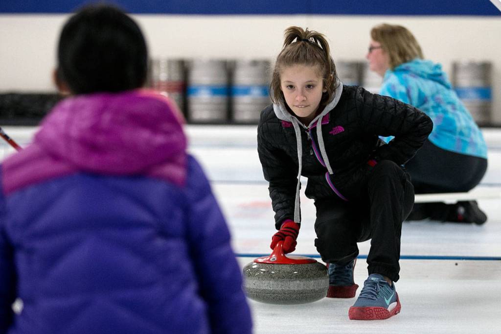 Sole Norman (right) practices rotating a rock to Ruby Kerwin during an open house at the Granite Curling Club on Feb. 18. (Kevin Clark / The Daily Herald)