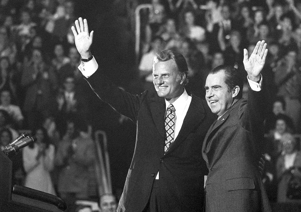 In this Oct. 16, 1971 photo, Evangelist Billy Graham and President Nixon wave to a crowd of 12,500 at ceremonies honoring Graham at Charlotte, North Carolina. (AP Photo, File)