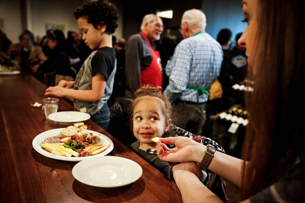 Alivia Broady (center), 3, gives her mom, Shauna (right), a look after being offered a piece of artisanal cheese along with her brother Bronson (left), 6, during Farms & Markets grand opening celebration in Everett on March 1. (Ian Terry / The Herald)