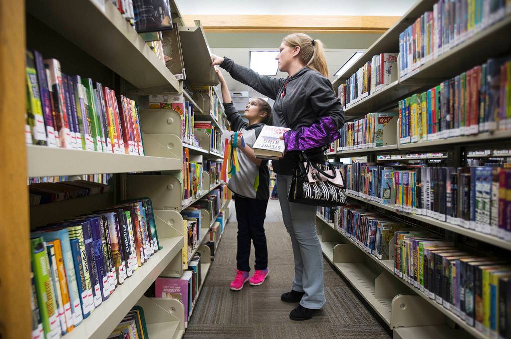 Jamie Thomas and daughter Nina Garcia look for books among the tightly spaced shelves at the Everett Public Library Evergreen Branch on March 5. (Andy Bronson / The Herald)