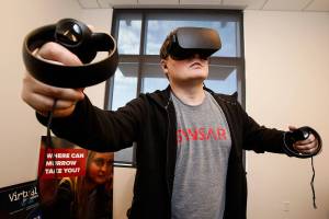 In his office at WSU Everett, clinical associate professor Brett Atwood, an expert with VR technology, dons an Oculus headset. (Dan Bates / The Herald)