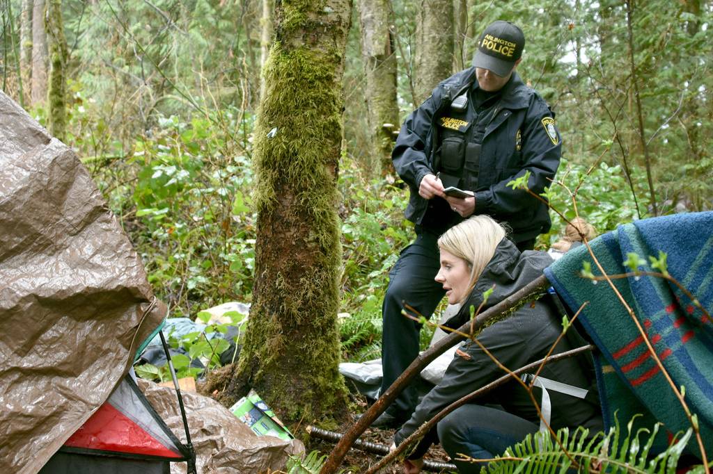 Marysvilles embedded social worker, Rochelle Long, speaks with a homeless couple living in the woods behind an apartment complex on Thursday. She started working for the city earlier this week. Arlington police officer Ken Thomas takes notes. (Caleb Hutton / The Herald)