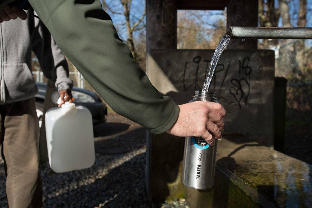 Paul Jung fills one of two water bottles at the artesian well on 164th Street on Monday, April 2, 2018 in Lynnwood, Wa. Jung who lives in Oak Harbor, says he always stops by if he is in the area. (Andy Bronson / The Herald)