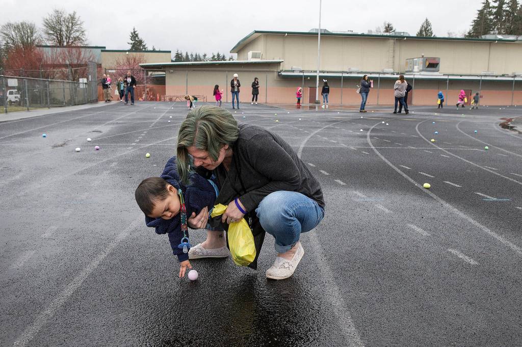 Nicole Lempke helps Giovanni Valentine grab an egg as they and other pre-school students hunt for eggs on the track at Granite Falls Middle School on March 29. About 45 students organized a morning of activities, including a petting zoo, games and the hunt. (Andy Bronson / The Herald)