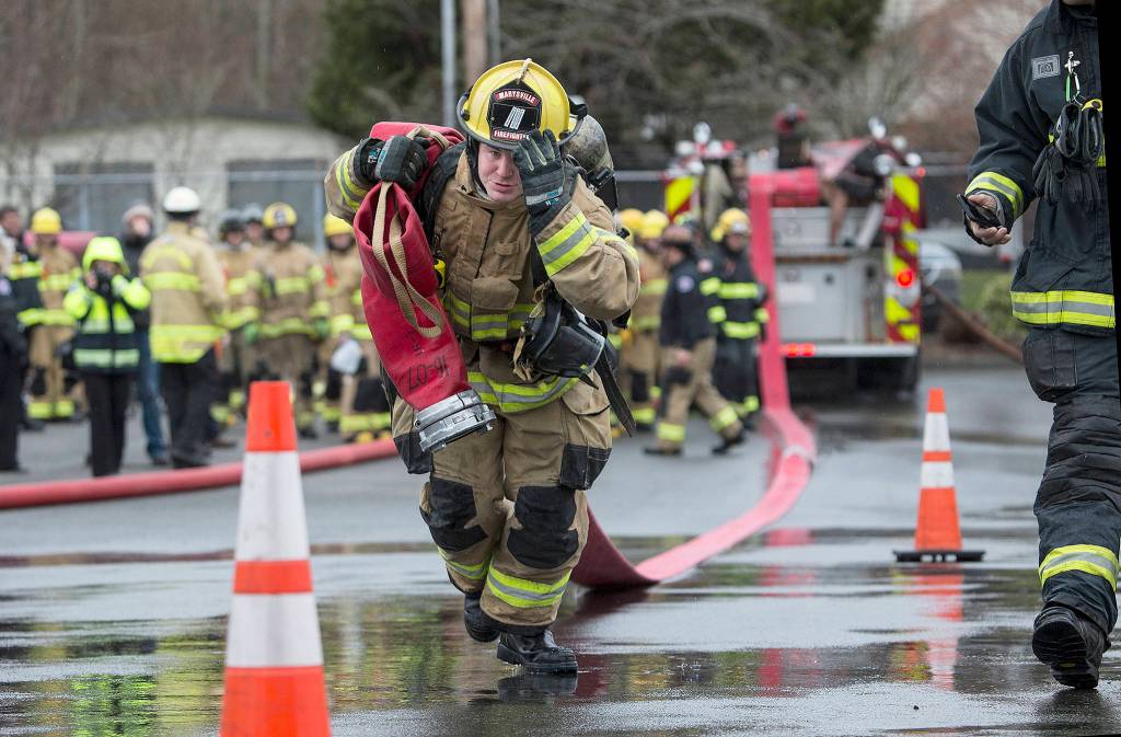 Marysville fire training recruit Brian Donaldson holds onto his helmet as he drags a 5-inch line 200 feet through an obstacle course at the South Snohomish Fire & Rescue training ground on March 26 in Everett. (Andy Bronson / The Herald)