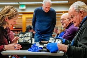 From left, library historian Lisa Labovitch, Jerry Solie (standing), and history buffs Dave Ramstad and William Vincent (right) enjoy one anothers light conversation while studying images in dozens of scrapbooks and photo albums Tuesday night at the Everett Public Library. (Dan Bates / The Herald)