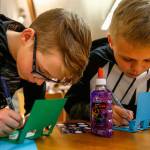 Carter Howell, 12 (left), from Post Middle School, and Bjorn Gudgeon, 12, from Haller Middle School, print messages on pop-up cards they made during a card-making party at Arlington Library on April 12. The cards were to be sent to the nonprofit Cards for Hospitalized Kids. (Dan Bates / The Herald)
