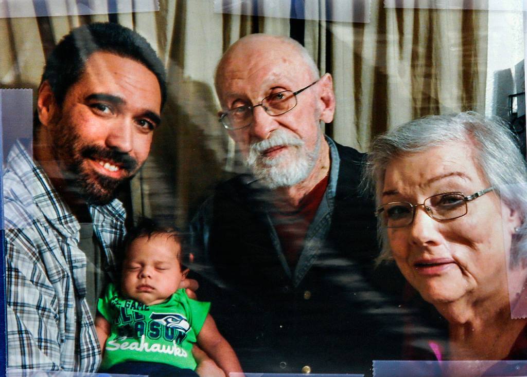 A family photo of John McKee (center) was displayed on a sign during Fridays tribute in downtown Everett. He is shown with his grandson, Keoni McKee (left), great-grandson Lucas and his wife, Audrey.