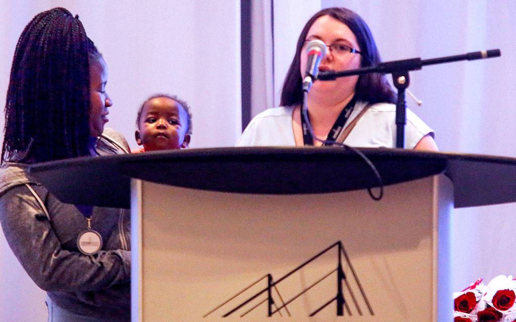 Baby Destiny, 10 months old, peeks out at the crowd while her mom, 17-year-old Valencia Saintilus, and Cocoon House staff member Echo Westfall stand at the podium during the Butterfly Celebration. (Dan Bates / The Herald)