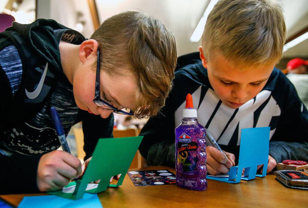 Carter Howell, 12, (left) from Post Middle School and Bjorn Gudgeon, 12, from Haller Middle School print messages on pop-up cards they made during a card-making party at Arlington Library April 12. The cards were to be sent to the nonprofit Cards for Hospitalized Kids. (Dan Bates / The Herald)