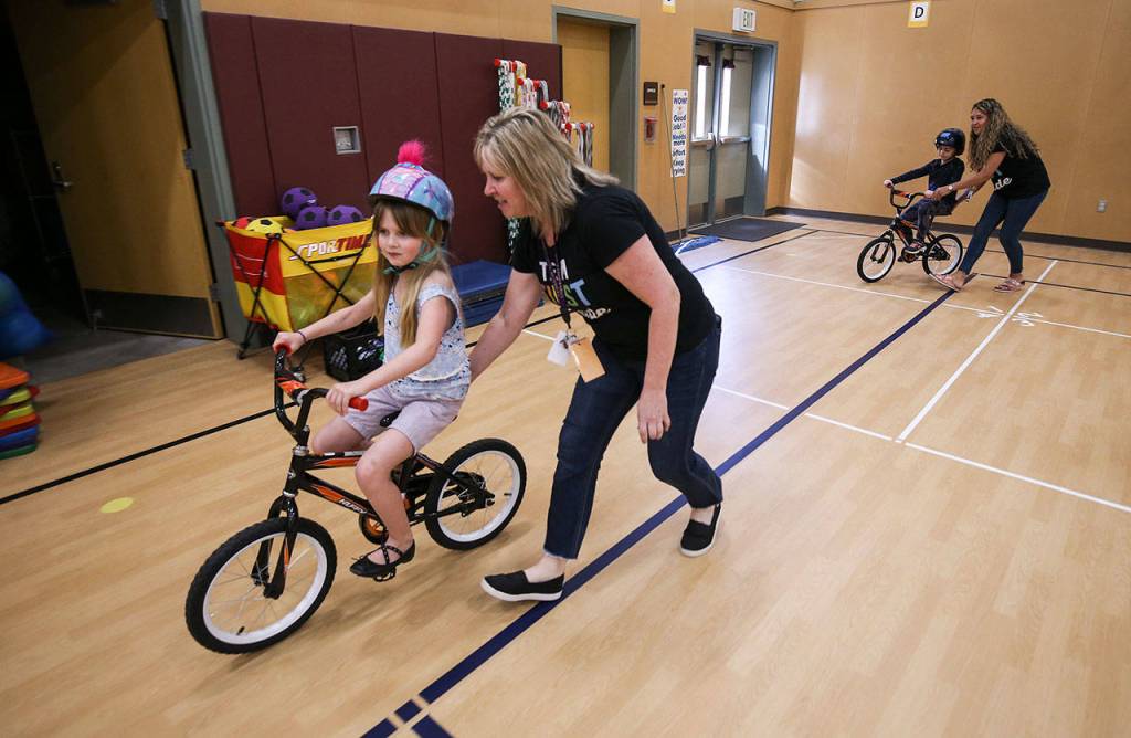 First-grader Lila Masters learns to ride bike with the help of Cassandra White (left), and Jasmine Lambert assists Lily Solerno-Blake in the gym at Silver Lake Elementary on Wednesday in Everett. (Andy Bronson / The Herald)