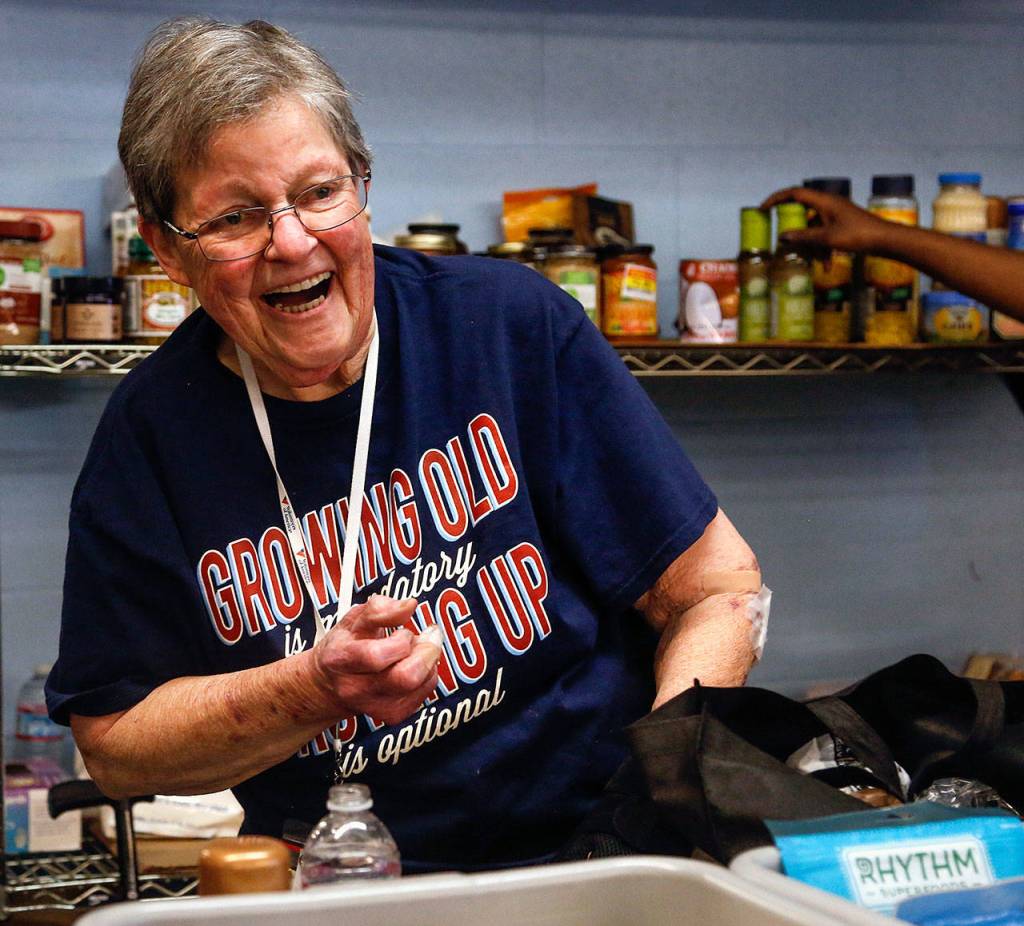 Pat Reeve, 78, who has volunteered there for 10 years, laughs with visitors Wednesday at the Everett Food Bank. (Dan Bates / The Herald)
