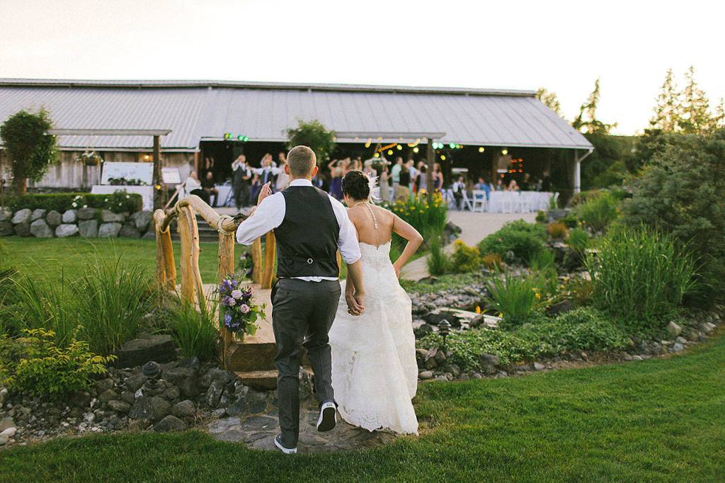 A groom and bride run over a bridge at Swan Trail Farms in Snohomish. (Rhys Logan Photography)