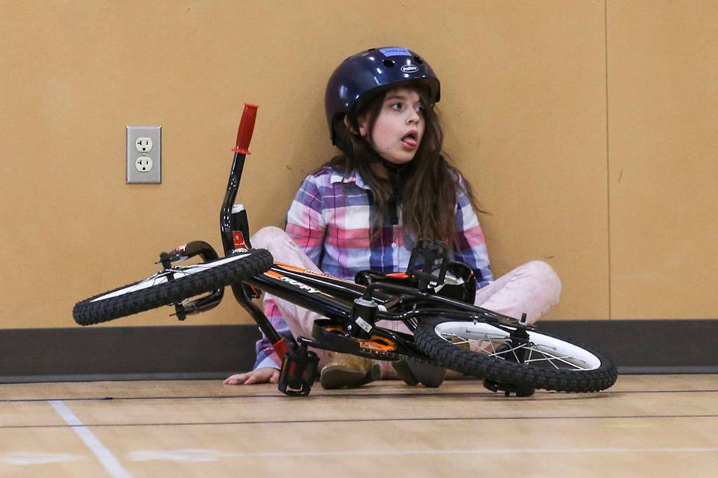 First grader Savannah Hartman gives an exasperated reaction to hitting a wall while learning to ride a bike in the gym at Silver Lake Elementary on May 9 in Everett. (Andy Bronson / The Herald)