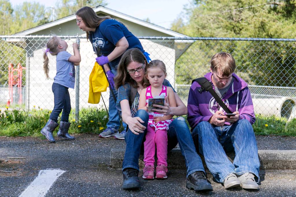 Cecilia Lasby (left) offers up a dandelion to her mother, Krista Lasby, as Kayla Nelson (holding Zooey Nelson and Sam Nelson) play a Pokemon Go Raid Battle at Osprey Park in Sultan on May 5. (Kevin Clark / The Herald)