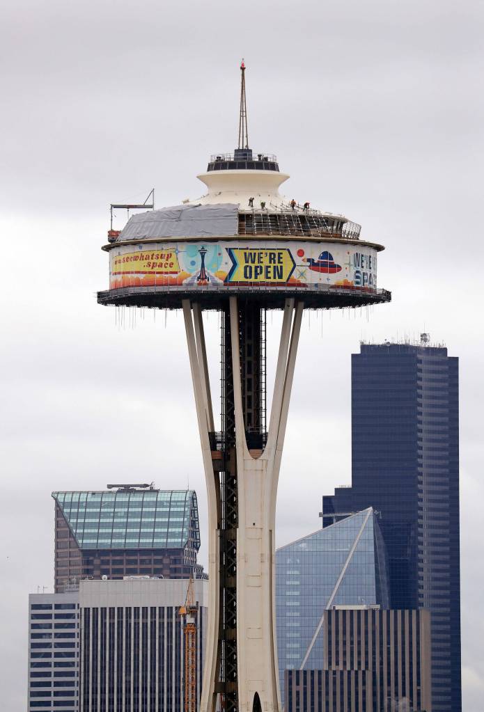 In this Feb. 7 photo, workers climb atop the roof of the Space Needle, where most of the top is surrounded by a massive work platform, scaffolding and protective covering, as work on a major remodel of the iconic observation tower continued in Seattle. (AP Photo/Elaine Thompson, file)