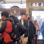 The final customers of the day line-up inside the Pike Place Market Starbucks, commonly referred to as the original Starbucks, after the doors were shut behind them Tuesday in Seattle. Starbucks closed more than 8,000 stores nationwide Tuesday to conduct anti-bias training. (AP Photo/Elaine Thompson)