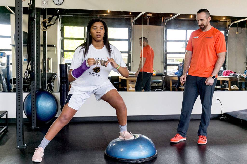 Kia Crawford (left) works through physical therapy under the watchful eye of Jared Appleby on May 9, 2018, at Experience Momentum in Lynnwood. (Kevin Clark / The Herald)