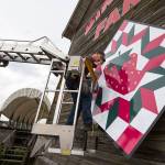 Scott Hines, of Marshall Signs, uses his foot to hold up the second half of a barn quilt during installation at Biringer Farm on June 8 in Arlington. (Andy Bronson / The Herald)
