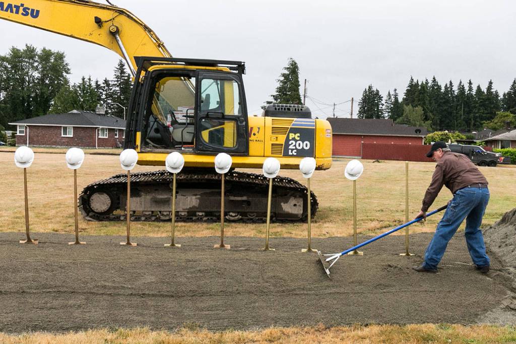 Tom Browne rakes the sand in preparation for the groundbreaking ceremony Saturday morning at the site of the new Everett Family YMCA. (Kevin Clark / The Herald)