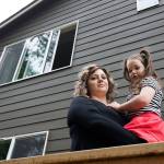 Kate Hitter holds her youngest daughter, Scarlett, under a third-story window at their Lake Stevens home on May 1 in Lake Stevens. While the family was moving in in 2017, Scarlett fell through a screened window and landed on the concrete patio 30 feet below. (Andy Bronson / The Herald)